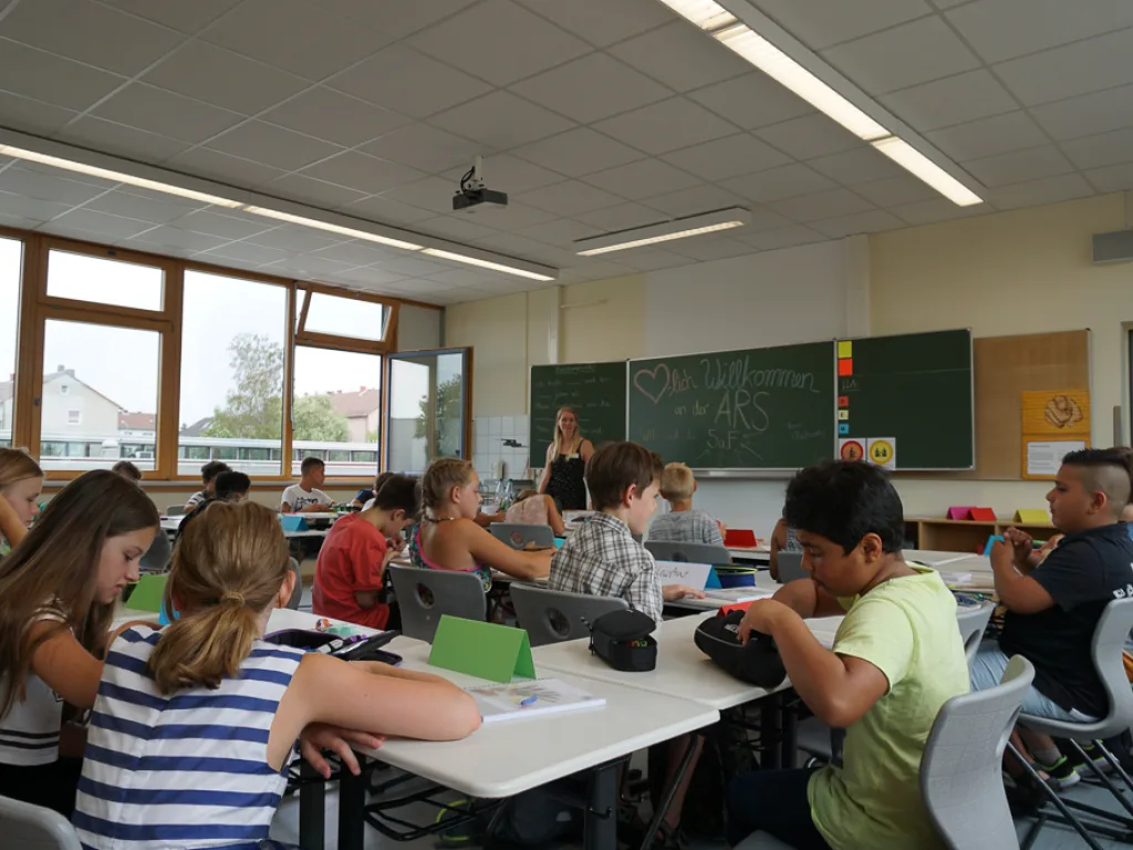 Kinder sitzen an Gruppentischen im Klassenraum.